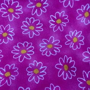 May include: A pink fabric with a white daisy pattern. The daisies have yellow centres.
