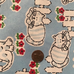 Może przedstawiać: Niebieski materiał z powtarzającym się wzorem białych kotów, czerwonych kwiatów i białych płotów. Materiał jest fakturowany i ma vintage'owy charakter.