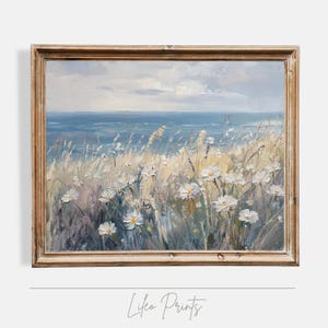 Puede incluir: Una pintura al óleo enmarcada que representa un paisaje marítimo con flores blancas en primer plano y un océano azul en el fondo. La pintura está enmarcada en un marco de madera marrón claro.