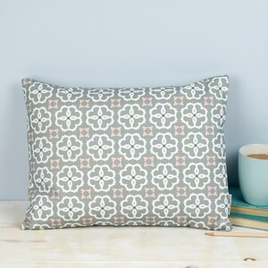 May include: A gray and white patterned throw pillow with pink accents. The pillow has a geometric design with a repeating pattern of flowers.