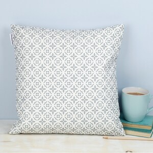 May include: A white throw pillow with a gray geometric pattern. The pillow is sitting on a table with a blue mug and books.