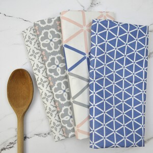 May include: Set of five kitchen towels with geometric patterns. The towels feature a variety of colors, including blue, pink, and gray. The towels are made of a soft, absorbent fabric.