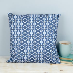 May include: A blue and white geometric patterned throw pillow. The pillow is on a white surface with a blue wall in the background.