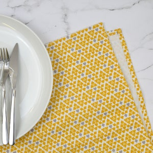 Peut inclure: Une assiette en c&eacute;ramique blanche avec trois fourchettes argent&eacute;es et un couteau argent&eacute; sur un set de table &agrave; motifs jaunes et gris.