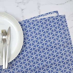 May include: A white dinner plate with two silver utensils and a clear glass sits on a blue and white geometric patterned tablecloth.