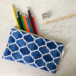 May include: A blue and white patterned pencil case with a zipper closure. The case is filled with colored pencils and a pencil sharpener.