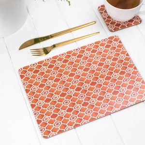 May include: Orange and white geometric patterned placemat with gold silverware on a white table.