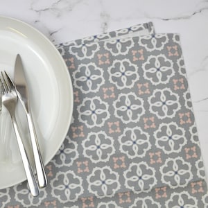 May include: A gray and white placemat with a pink and blue geometric pattern. A white plate and silverware are on top of the placemat.