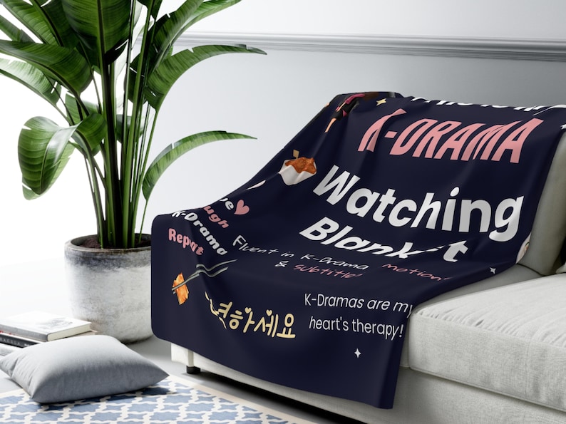 K-Drama Watching Blanket draped over a couch, showcasing fun K-Cozy K-Drama blanket with quotes like "Live Laugh K-Drama Repeat" and "K-Dramas are my heart's therapy!" Perfect for fans, surrounded by comfy decor.