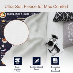 May include: A white fleece blanket with a black and white print featuring the text "Just one more K-drama episode!" and a heart with the text "Live Laugh K-Drama Repeat". The blanket is folded in half and has a white background with a black border. The blanket is shown on a white surface with a black and white patterned pillow and a gray pillow with a floral design. The blanket has double-stitched edges and a fade-resistant print.