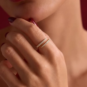 May include: A gold-toned open ring featuring two tapered ends, each encrusted with a row of small, clear, sparkling stones. The band is split, allowing the two pointed ends to overlap slightly on the finger, creating a sleek and continuous design.
