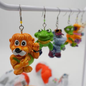 Peut inclure: Une collection de boucles d'oreilles fantaisie colorées représentant des personnages d'animaux de dessins animés. Les boucles d'oreilles comprennent un lion, une grenouille, un hippopotame et d'autres personnages.