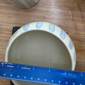 May include: A ceramic bowl with a speckled cream-colored interior and exterior. The rim is decorated with vertical light blue stripes. The bowl measures approximately 5 inches in diameter.