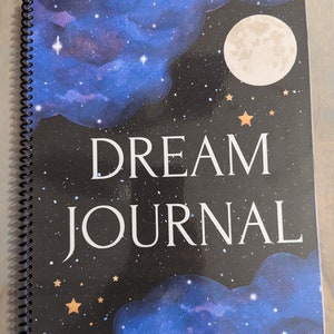 May include: A black and blue spiral bound journal with a galaxy design. The cover features a large white moon, stars, and the text "DREAM JOURNAL".