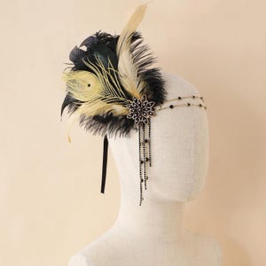 May include: A vintage-style headband featuring black, cream, and peacock feathers. The headpiece includes a decorative flower with dangling black beads and a gold-toned double-strand band. A black ribbon secures the headband.