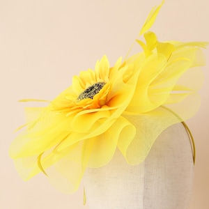 May include: A vibrant yellow sunflower headpiece with a black centre and delicate yellow feathers. The headpiece features a ruffled tulle design and is attached to a thin headband. Ideal for special events.