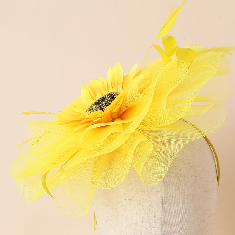 May include: A vibrant yellow sunflower headpiece with a black centre and delicate yellow feathers. The headpiece features a ruffled tulle design and is attached to a thin headband. Ideal for special events.