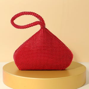 Op de afbeelding: Een felrode handtas bedekt met kleine, uniforme kralen. De tas heeft een opvallend driehoekig silhouet met een enkele ge&iuml;ntegreerde ronde handgreep aan de bovenkant, die ook volledig is versierd met bijpassende rode kralen voor een textuurrijk oppervlak.