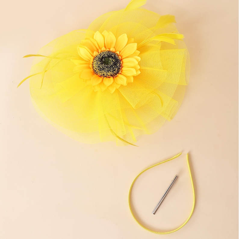 May include: A vibrant yellow hair accessory with a sunflower and tulle design. The sunflower has a dark centre and yellow petals. A matching yellow elastic band with a silver metal clip is also included.