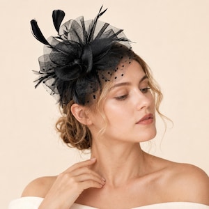 Può includere: Un copricapo fascinator nero caratterizzato da strati di tulle, un delicato velo a pois e piume decorative rivolte verso l'alto. L'accessorio è realizzato con una base strutturata e complesse pieghe di tessuto, creando un aspetto voluminoso e materico.