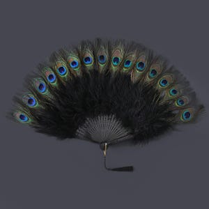 Peut inclure: Éventail noir orné de plumes de paon. Le ventilateur présente une poignée noire et une disposition décorative de plumes noires avec des plumes d'œil de paon vibrantes dans des tons de bleu, vert et or. Une gland noir est suspendu à la base.