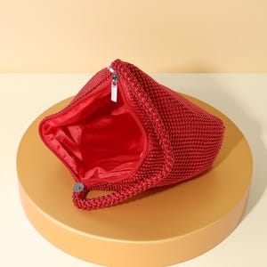 Op de afbeelding: Een felrode handtas bedekt met kleine, uniforme kralen met een getextureerd oppervlak. De tas heeft een enkel kralenhandvat en een zilverkleurige metalen ritssluiting aan de bovenkant. De binnenkant is gevoerd met bijpassende rode stof, zichtbaar door de opening.