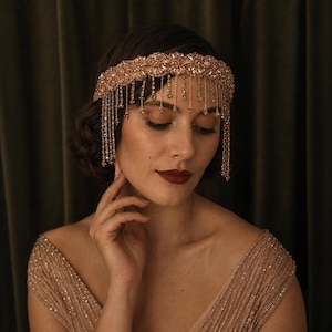 May include: A rose gold tone headband featuring a wide, intricate band of sparkling crystals and beads. The accessory includes multiple dangling crystal fringe strands that hang down over the forehead, creating a layered, shimmering effect.
