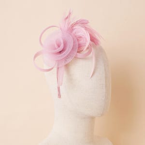 Peut inclure: Un fascinateur rose clair avec une fleur en résille et des plumes. Le couvre-chef présente une fleur en résille superposée, complétée par des rubans incurvés et des plumes douces. Un accessoire élégant pour les occasions spéciales.