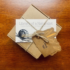May include: A small brown box wrapped in twine with a tag that says "Thank You!" and a card that says "Library of a Naturalist, Curated Natural History Books and Curiousities" with a drawing of a snail.