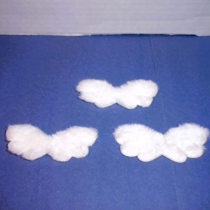 May include: Three fluffy, white, cloud-shaped decorations are arranged on a blue surface. Each cloud has a rounded, textured appearance, suggesting a soft, plush material. The background is a solid, deep blue.