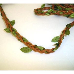 May include: Braided brown vine garland with green fabric leaves. The garland is made of a woven brown material with green leaves attached at intervals. The leaves are a bright green color and add a natural touch to the garland.