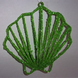 May include: A bright green, glitter-covered seashell ornament. The openwork design features radiating lines, creating a shell shape. The ornament has a loop for hanging, perfect for holiday or coastal decor.