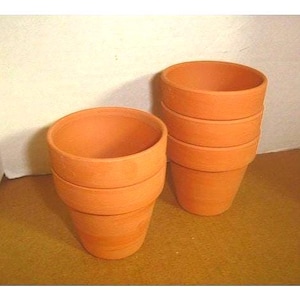 May include: A collection of terracotta flower pots. The pots are stacked, showcasing their cylindrical shape with a slightly flared rim. The unglazed clay has a warm, orange-brown hue. The pots are suitable for planting flowers or herbs.