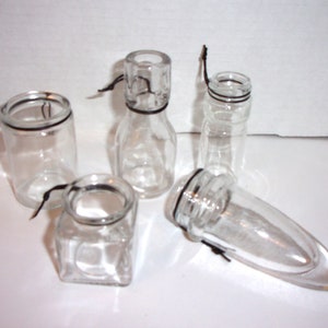 May include: Five clear glass bottles with black string ties. The bottles are various shapes and sizes.