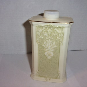 May include: A white ceramic bottle with a gold trim and a white floral design. The bottle has a white plastic lid.