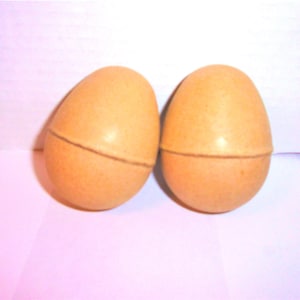 May include: Two light brown, egg-shaped containers. Each has a horizontal line circling the middle. The containers are on a white and pink surface. The eggs are side by side.