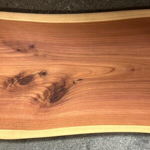 May include: A large, natural wood serving board with a live edge and a wavy shape. The board has a reddish-brown color and a natural wood grain pattern.