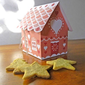 May include: A pink and white gingerbread house with a white heart on the front and a red door. The house is decorated with white dots and hearts. There are four star-shaped cookies on a wooden surface in front of the house.
