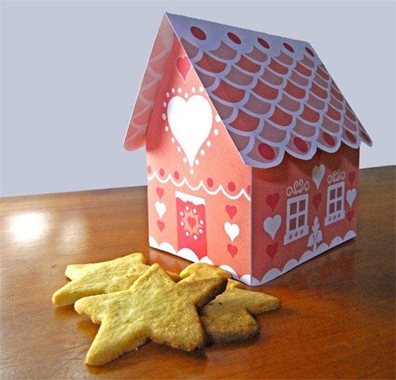 May include: A pink and white gingerbread house with a heart-shaped window and red polka dots. The house is sitting on a wooden surface with star-shaped cookies.