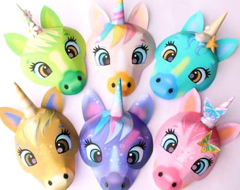 May include: Six colorful paper unicorn masks with different colored horns, eyes, and details. The masks are all facing forward and have a 3D effect.