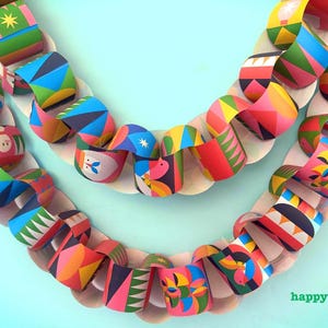 May include: Colorful paper chain garland with geometric and floral patterns in shades of pink, blue, yellow, and green. The garland is arranged in a curved shape against a light blue background. The word "happythought" is visible in the bottom right corner.