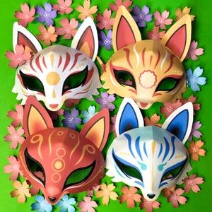 Puede incluir: Cuatro m&aacute;scaras japonesas kitsune de colores con dise&ntilde;os intrincados, sobre un fondo verde con flores de papel rosa y azul.