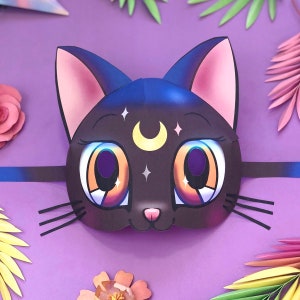 Puede incluir: Una máscara de gato negro con ojos grandes de dibujos animados y una luna creciente en la frente. La máscara está decorada con estrellas blancas y tiene un fondo morado.