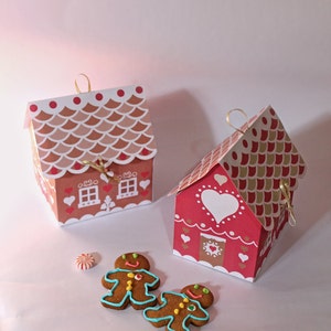 May include: Two red and white gingerbread house shaped boxes with gold ribbon and gingerbread men cookies.