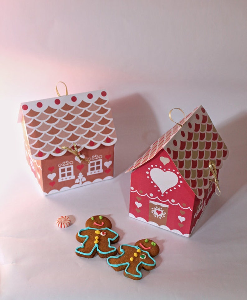 May include: Two red and white gingerbread house shaped boxes with gold ribbon and gingerbread men cookies.