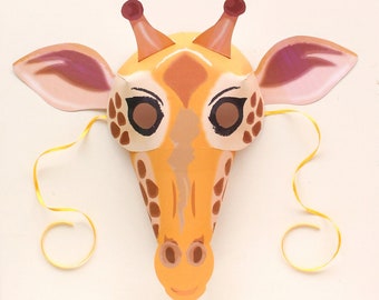 May include: A yellow and brown giraffe mask with pink ears and a yellow string attached. The mask has black eyes and a brown nose.