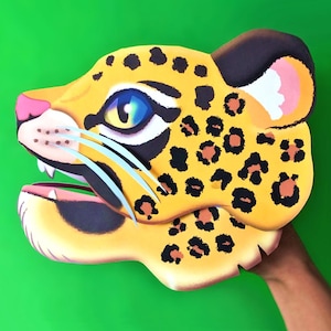 Könnte beinhalten: Eine gelbe und schwarze Jaguar-Puppe mit einer rosa Nase und blauen Augen. Die Puppe ist aus Papier und hat einen ausgeschnittenen Mund.