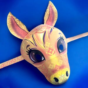 Può includere: Una maschera decorativa a forma di cavallo dal design stravagante. La maschera presenta una base giallo chiaro con accenti rosa e viola, ornata da motivi floreali e a spirale. Gli occhi sono grandi e scuri, con lunghe ciglia. La maschera ha lunghe orecchie e un manico a bastone.