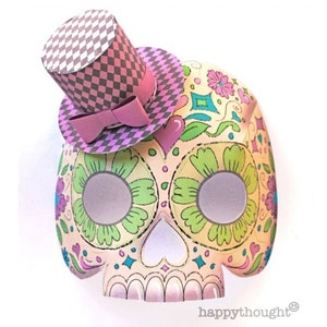 May include: A papercraft sugar skull mask with a pink and gray top hat. The mask is decorated with colorful flowers and patterns.