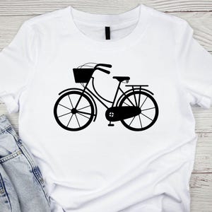 K&ouml;nnte beinhalten: Ein wei&szlig;es T-Shirt mit einer schwarzen Silhouette eines Fahrrads mit einem Korb vorne.